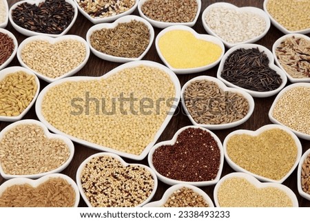Large cereal and grain food selection in heart shaped porcelain bowls over lokta paper background. Pearl couscous in large dish.
