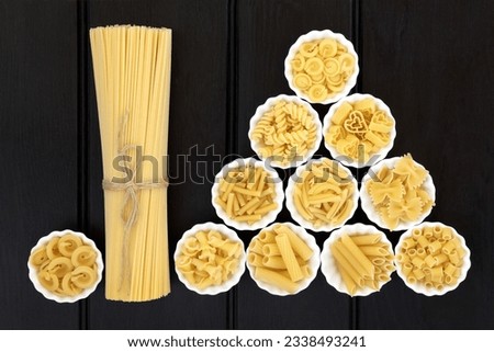 Spaghetti pasta dried food selection in a bundle and in porcelain crinkle bowls over dark wood background.