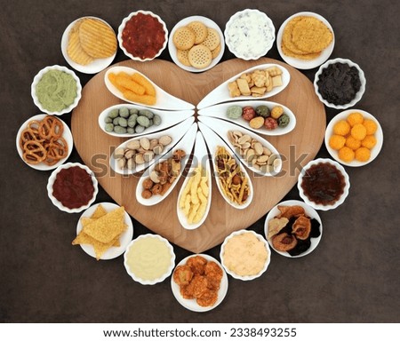 Savoury snack and dip party food selection in porcelain dishes on a heart shaped wooden board.