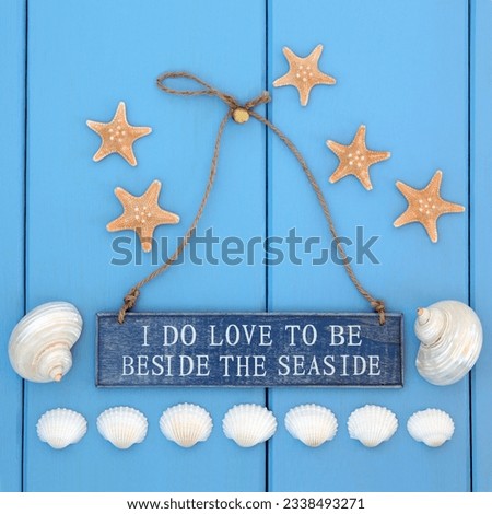 I do love to be beside the seaside sign, starfish, cockle and mother of pearl shells over wooden blue background.
