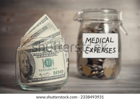 Dollars and coins in glass jar with medical expenses label, financial concept. Vintage tone wooden background with dramatic light.