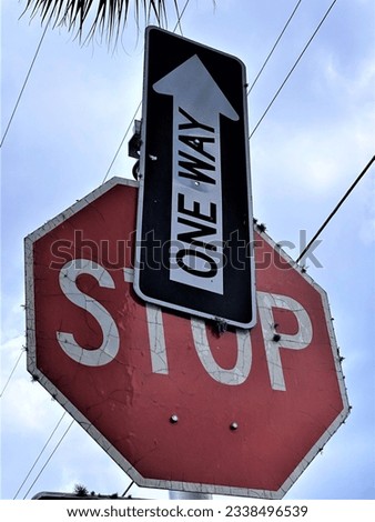 A STOP sign is partially blocked by a ONE WAY sign pointing straight upward. 