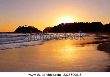 The golden sun rises behind the headland and detached island at Number One Beach, Seal Rocks NSW Australia. The beach is 1.3km long and curves around to face