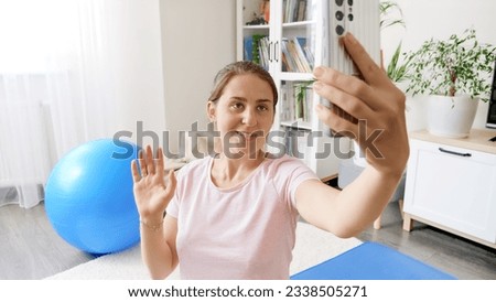 Portrait of young woman blogger talking to her audience in smartphone before doing fitness training in living room. Concept of healthcare, sports and yoga at home
