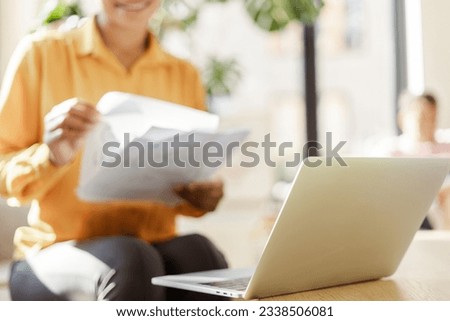 Beautiful smiling African American business woman, freelancer holding documents using laptop working online from home. Successful business 