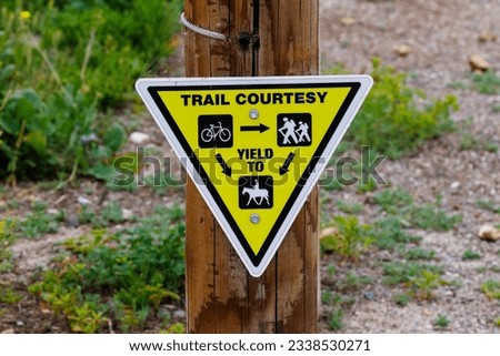 Triangular yellow trail courtesy sign on a wood post giving yield instructions