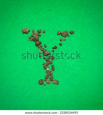 Alphabet Y made of arrangement of small stones or pebbles on green paper.