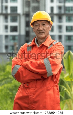 Portrait senior Japanese engineer in work jumpsuit and safety helmet standing arm crossed with high building background Royalty-Free Stock Photo #2338544265