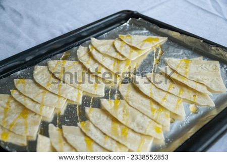 A baking sheet filled with tortilla chips, ready to be transformed into mouthwatering nachos in the oven, a perfect snack for any occasion. Royalty-Free Stock Photo #2338552853