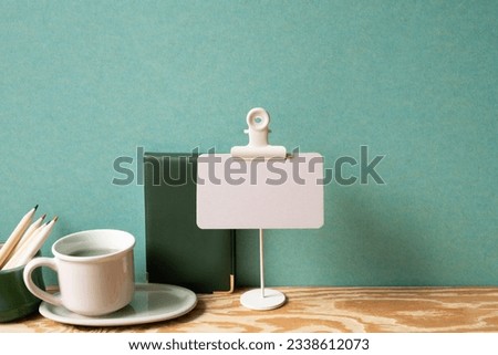 Memo pad, note, cup of tea, colored pencil on wooden desk. green wall background. study and workspace. copy space Royalty-Free Stock Photo #2338612073