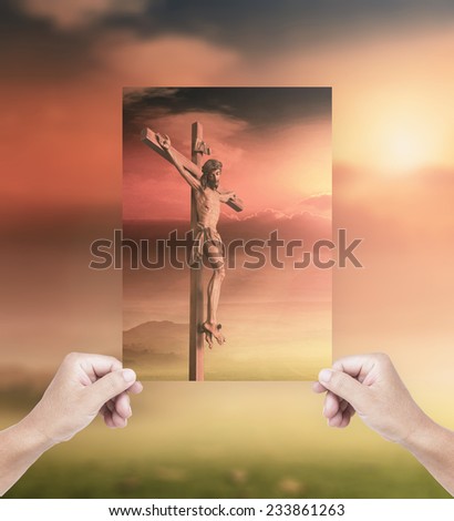 Human hands holding picture Jesus christ on the cross over a sunset background.