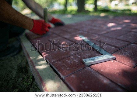 The protractor lies on the paving stones and the worker lays the pavement.