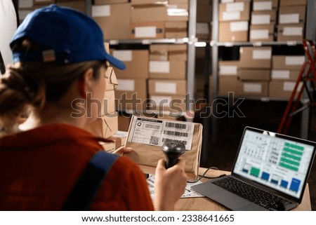 Woman worker working with warehouse management system with barcode reader and laptop computer. Girl working in factory warehouse scanning labels on the boxes with barcode scanner. Close-up Royalty-Free Stock Photo #2338641665