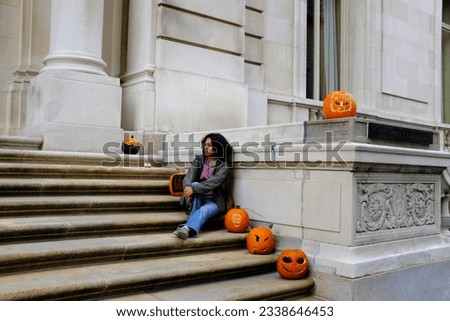 An Asian female tourist sitting on a large stairs with head of Jack-o'-lantern during the Halloween season in New York City.