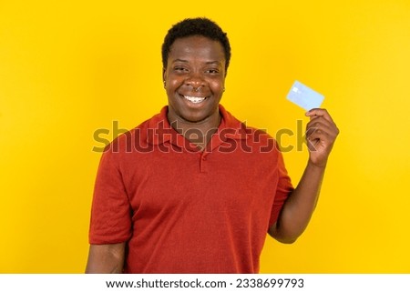 Photo of happy cheerful smiling positive Young latin man wearing red T-shirt over yellow background recommend credit card