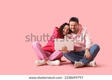 Young couple using laptop on pink background