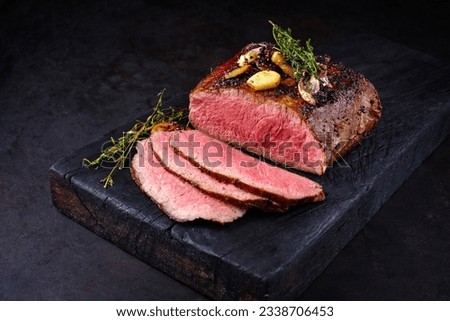 Traditional Commonwealth Sunday roast with sliced cold cuts roast beef with garlic and salt as close-up on a rustic charred wooden board  Royalty-Free Stock Photo #2338706453