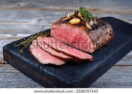 Traditional Commonwealth Sunday roast with sliced cold cuts roast beef with garlic and salt as close-up on a rustic charred wooden board  Royalty-Free Stock Photo #2338707143