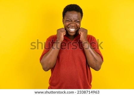 Young latin man wearing red T-shirt over yellow background grins joyfully, imagines something pleasant, copy space. Pleasant emotions concept. Royalty-Free Stock Photo #2338714963