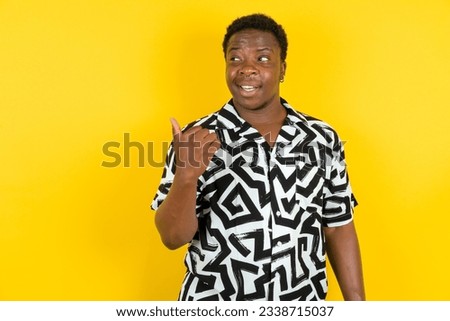 Young latin man wearing printed shirt over yellow background points away and gives advice demonstrates advertisement