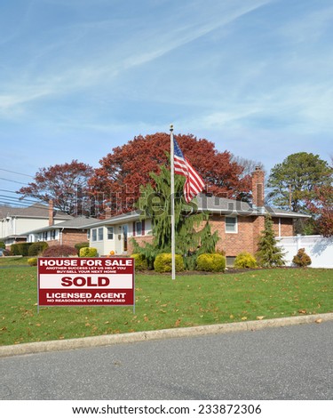 American flag pole Real Estate Sold (another success let us help you buy sell your next home) sign suburban ranch style home autumn season day residential neighborhood blue sky clouds USA