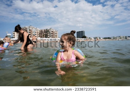 Little girl swims in the sea with the help of an inflatable ring.