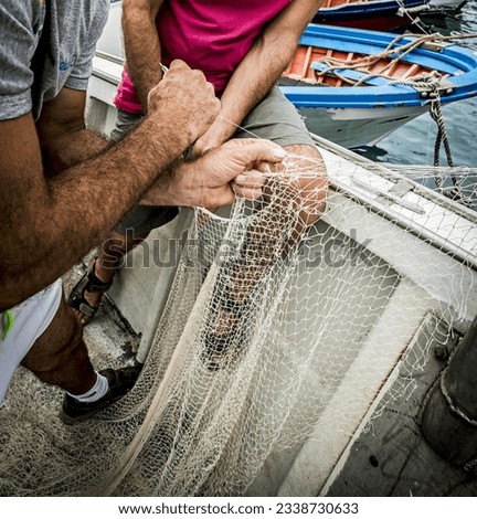 Italy, Sicily, Mediterranean sea, Catania; fisherman repairing his nets on a fishing boat in the port.