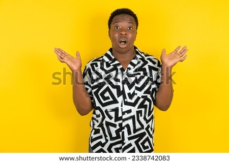 Surprised terrified Young latin man wearing printed shirt over yellow background Gestures with uncertainty, stares at camera, puzzled as doesn't know answer on tricky question, People, body language, 