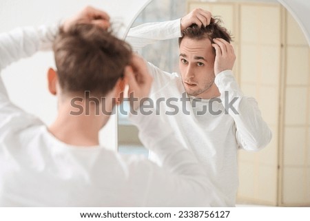 Young man with hair loss problem looking in mirror at home Royalty-Free Stock Photo #2338756127