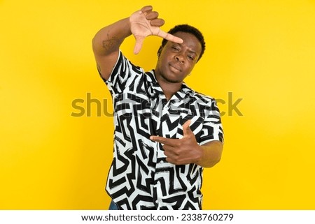 Young latin man wearing printed shirt over yellow background making finger frame with hands. Creativity and photography concept.