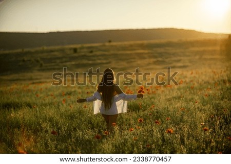 Woman sunset field. Happy woman walking in the field toward the sun holding a poppy flower.