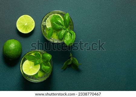 Fresh iced lemonade with basil and lime on dark green background top view, copy space for your design.