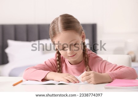 Girl using eraser at white desk in room