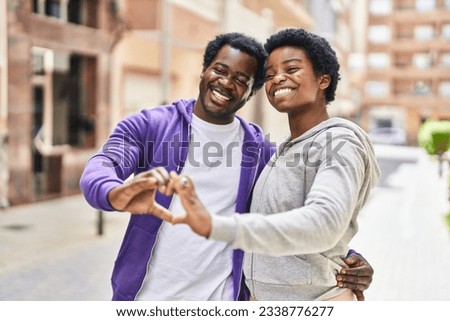 African american man and woman couple doing heart gesture at street