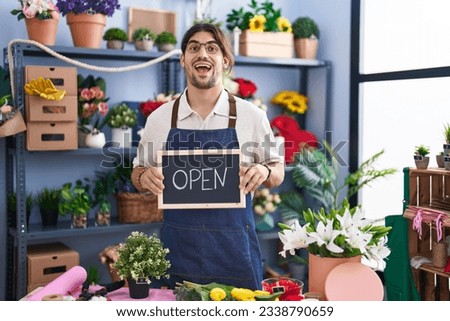 Hispanic man with long hair working at florist holding open sign celebrating crazy and amazed for success with open eyes screaming excited. 