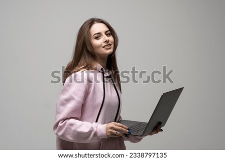 Attractive brunette woman 20s wearing pink hoodie standing working on laptop pc computer isolated on grey wall background studio portrait.