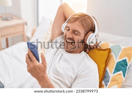 Young blond man watching video on smartphone lying on bed at bedroom