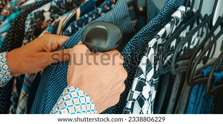 a man in a clothes shop using a barcode scanner to scan the information of a shirt in a hanger, in a panoramic format to use as web banner Royalty-Free Stock Photo #2338806229