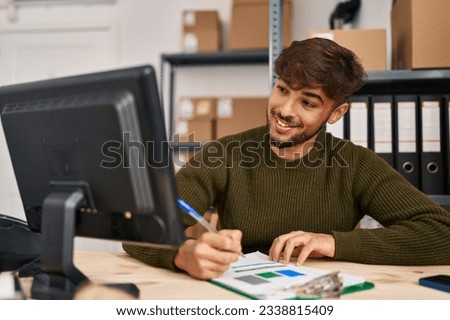 Young arab man ecommerce business worker writing on document using computer at office