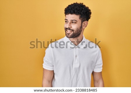 Arab man standing over yellow background looking away to side with smile on face, natural expression. laughing confident.  Royalty-Free Stock Photo #2338818485