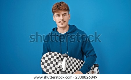 Young hispanic man holding skate standing with serious face over isolated blue background