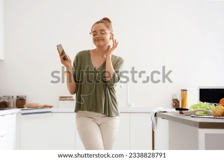 Pretty young woman listening to music and dancing in light kitchen