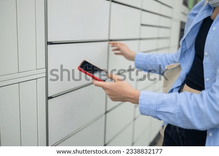 Beautiful woman picking up a package from a smart electronic steel parcel locker box, automatic mailboxes. Pachkomat delivery service, collection machine Royalty-Free Stock Photo #2338832177