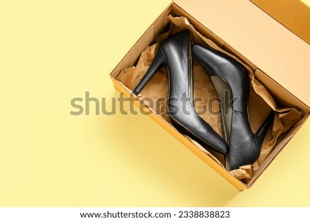 Cardboard box with high heeled shoes on beige background Royalty-Free Stock Photo #2338838823