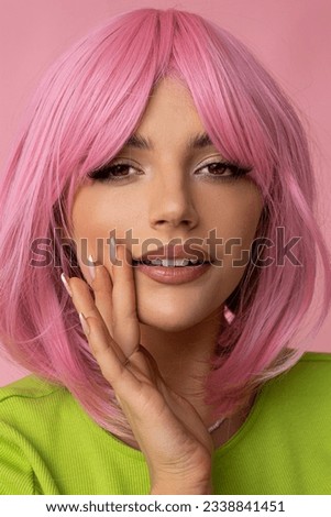 Cute young woman with pink hair and bright green dress on isolated pink background.
