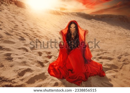 Mystery arabic woman sits in desert, gold mask veil accessories niqab burqa hide face. Fantasy girl art photo fashion model black hair head cover scarf, red long dress. Sand dunes sun light