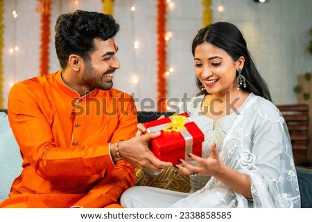 Happy young husband giving present to wife during festival celebration at home - brother giving gift to sister during raksha bandhan. Royalty-Free Stock Photo #2338858585