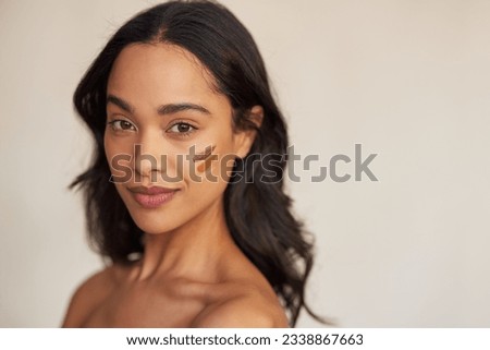 Portrait of young latin hispanic woman applying foundation swatches of various tone on face while looking at camera. Beautiful mixed race makeup artist with swatches of foundation cream on cheek. Royalty-Free Stock Photo #2338867663