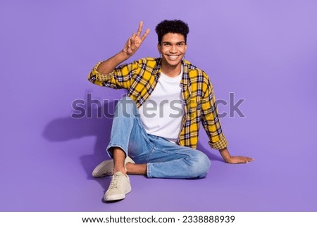 Full body photo of cheerful satisfied person sit floor hand fingers demonstrate v-sign isolated on violet color background
