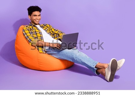 Photo of cheerful young man sit cozy bag use wireless netbook eshopping surfing isolated on violet color background